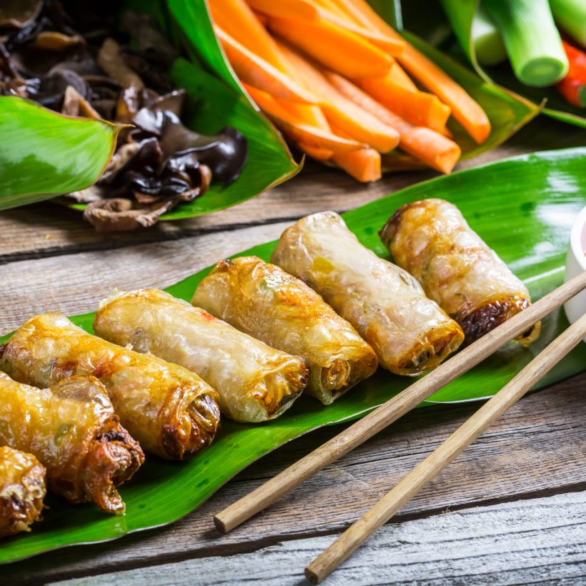 Fried spring rolls surrounded by ingredients on wooden table
